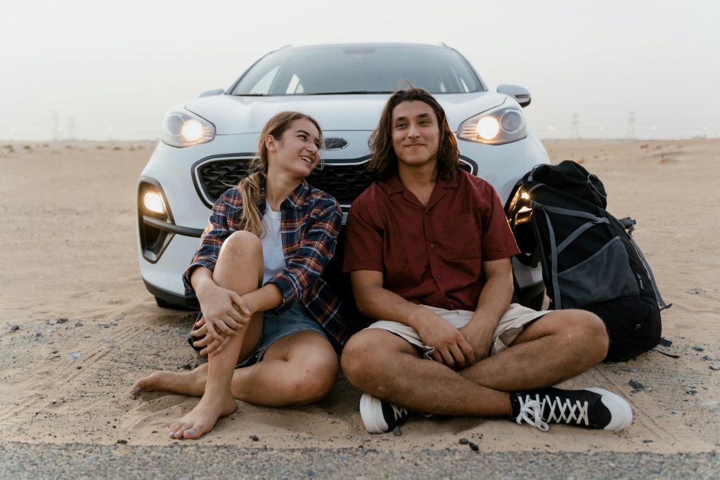 Should I get a car loan? Young couple on beach sit in front of a car they just bought.